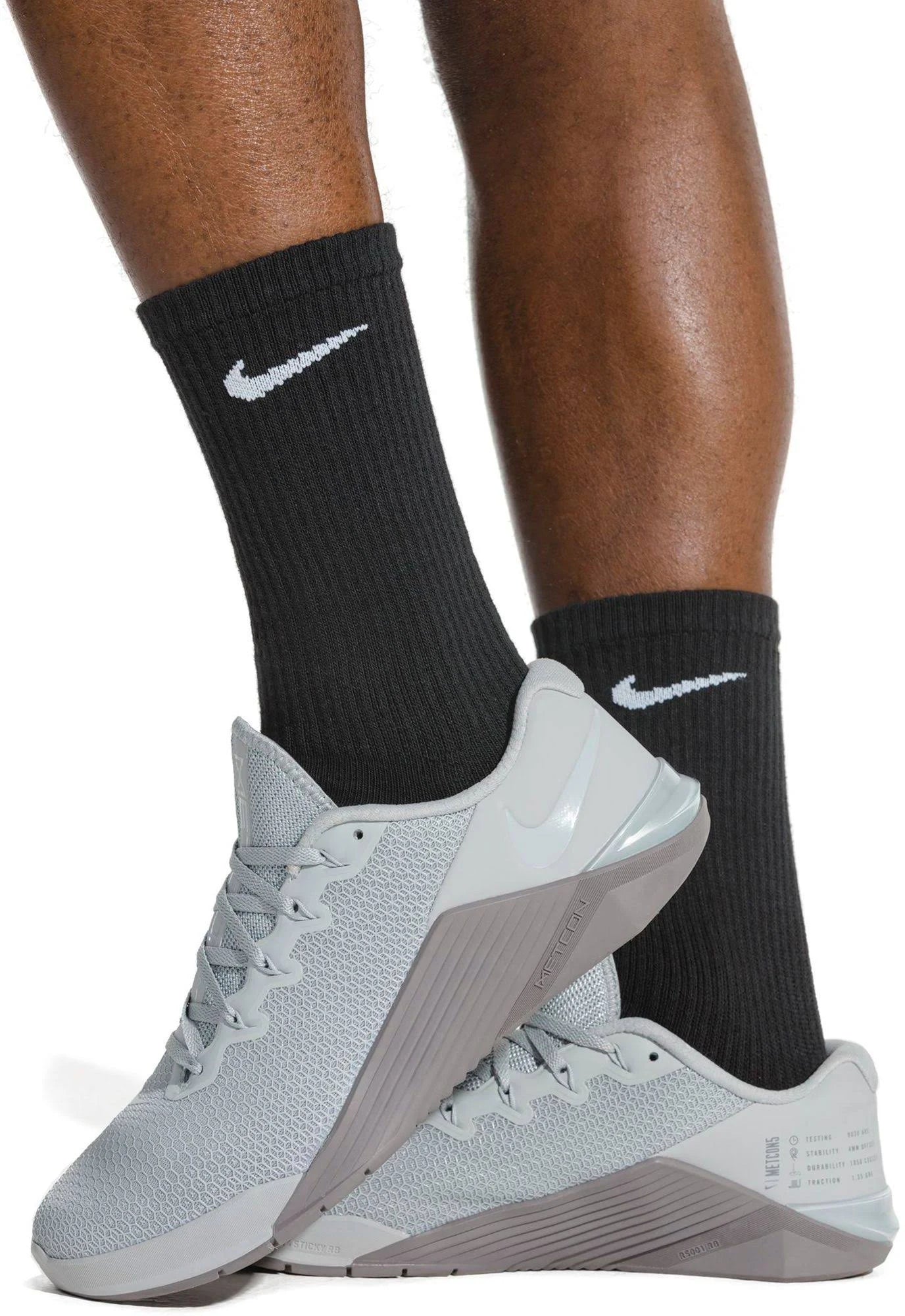 Person wearing black Nike Everyday Socks with white swoosh logo, paired with grey sneakers. Ideal for athletic and casual use.