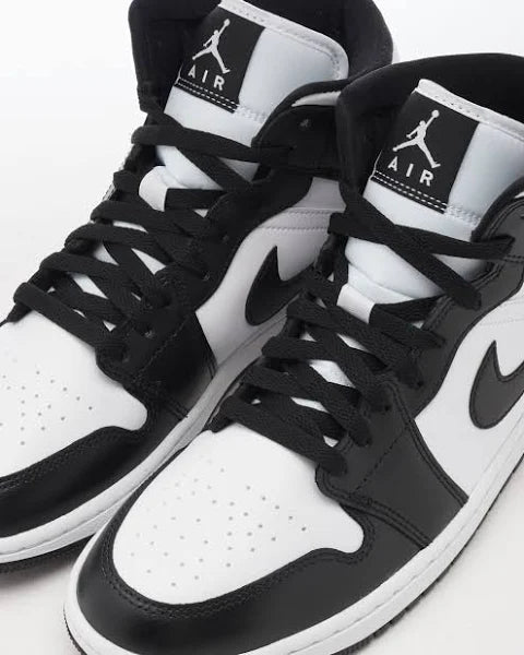 Jordan 1 Mid 'Panda' sneakers with black laces and Jumpman logo on the tongue, offering a classic and trendy look. Perfect for everyday wear.